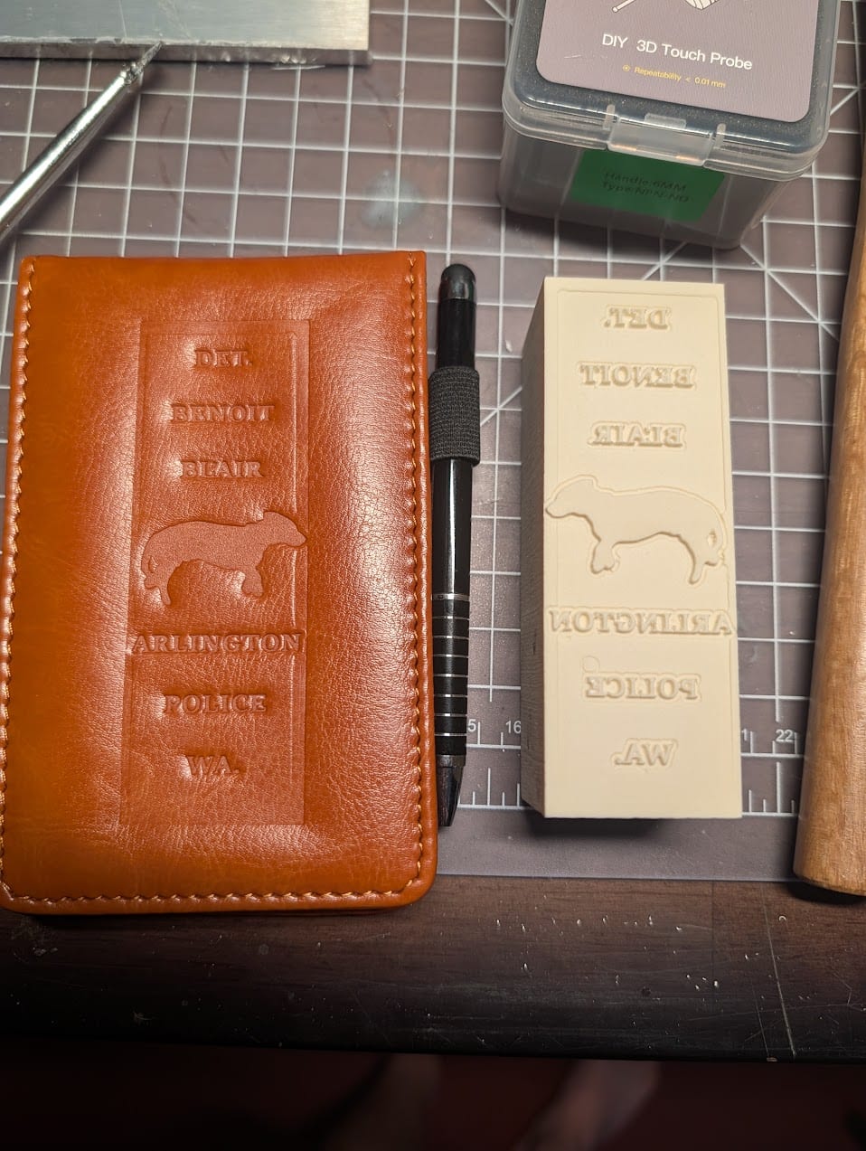 The brown notebook cover embossed with Detective Benoit Blair, a dog silhouette, and Arlington Police lettering, beside the mirrored epoxy block.