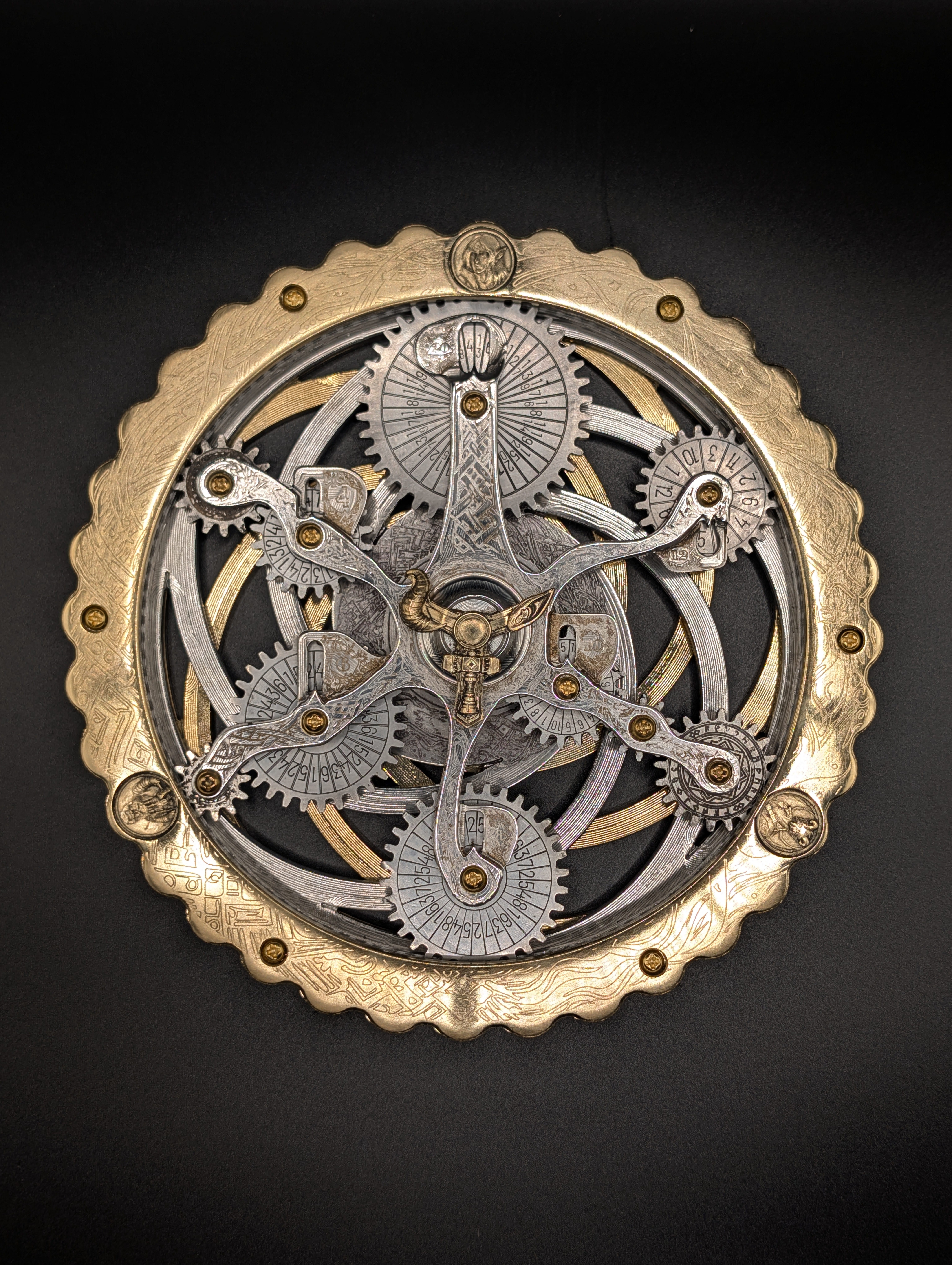 The finished Oracle photographed straight down on black: a scalloped brass ring around a silver gear train, five numbered dice wheels on curved arms, and a horned boss at the centre.