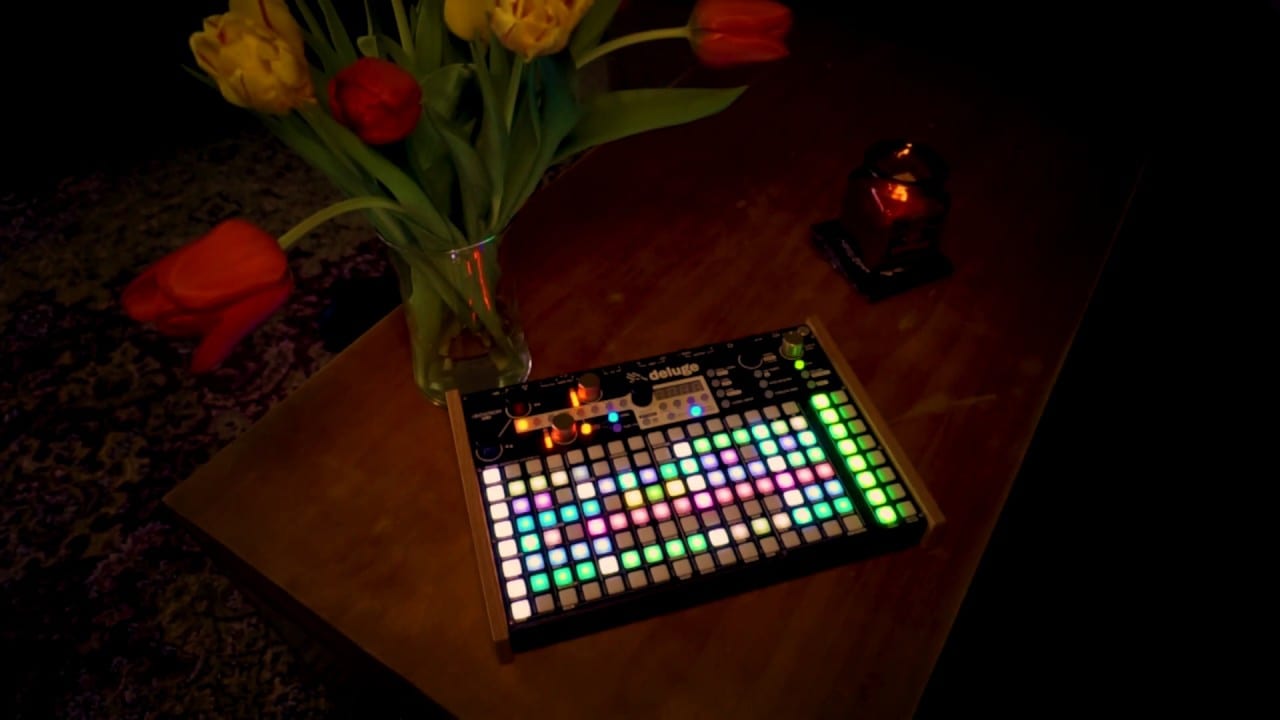 A lit Deluge on a wooden table beside a vase of red and yellow tulips.