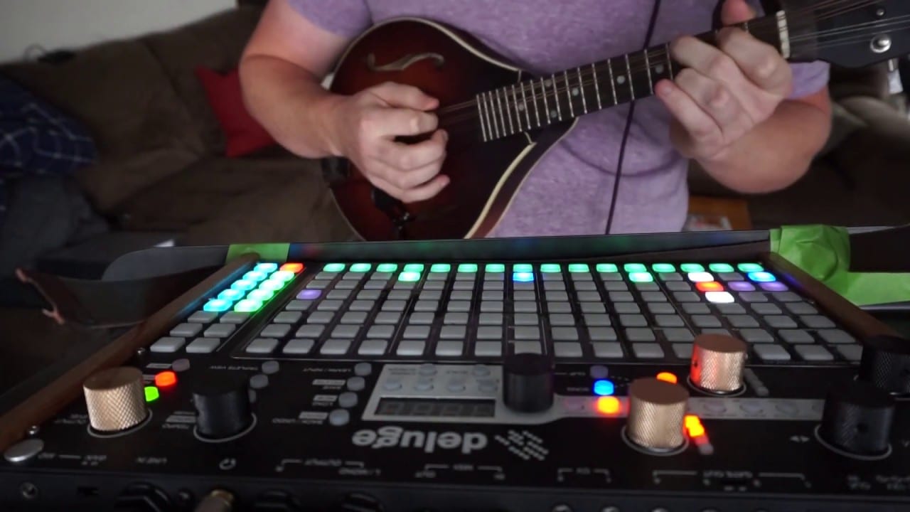 A person playing mandolin behind a Deluge with green and blue pads lit.