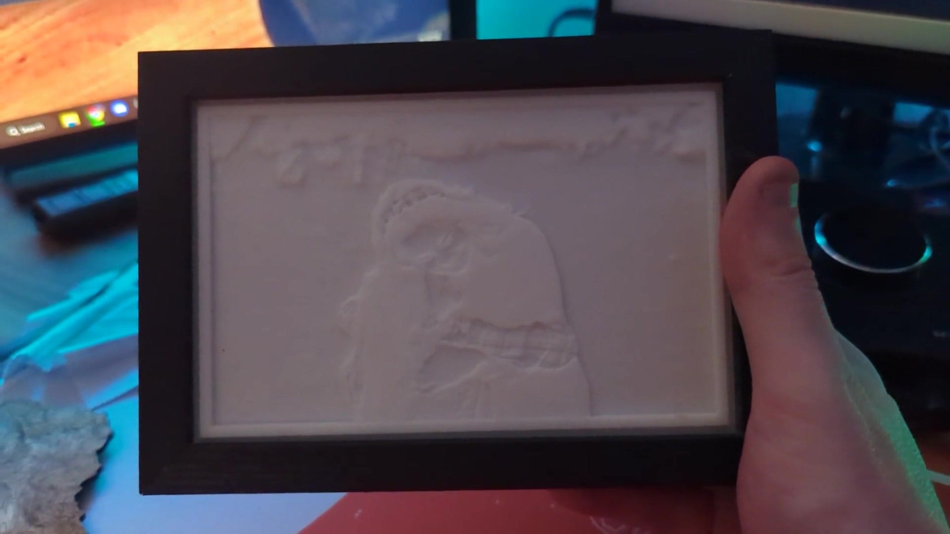 A small black shadow box held in one hand, containing an unlit white resin lithophane made from a family photograph.