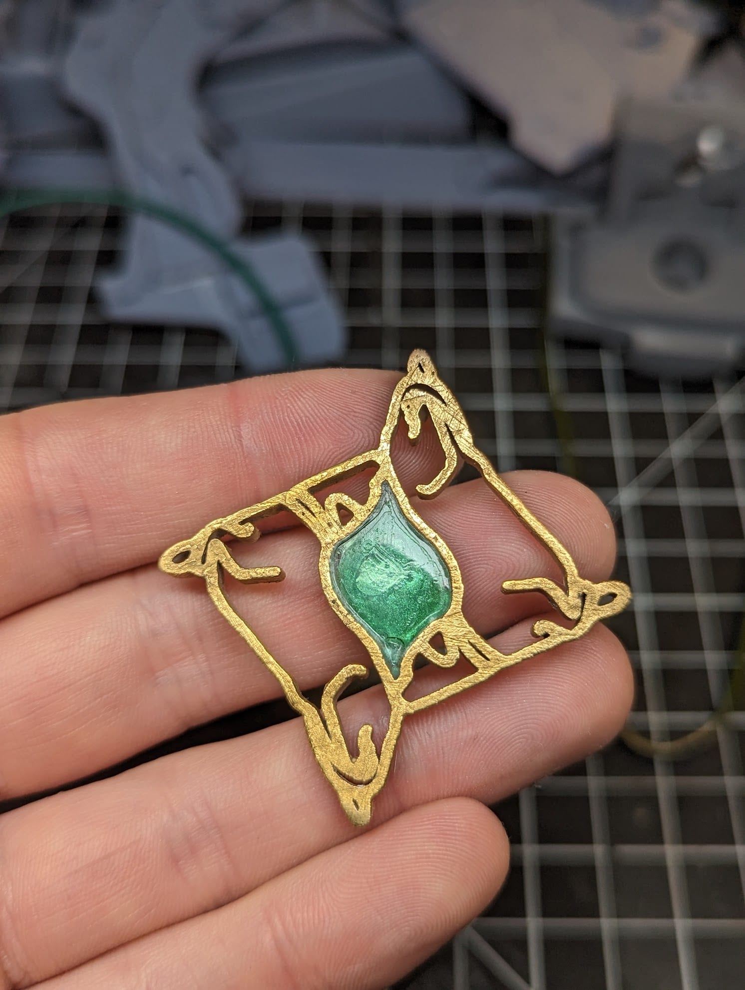 The finished gold dog-outline pendant held in one hand, with its center filled by translucent green resin.
