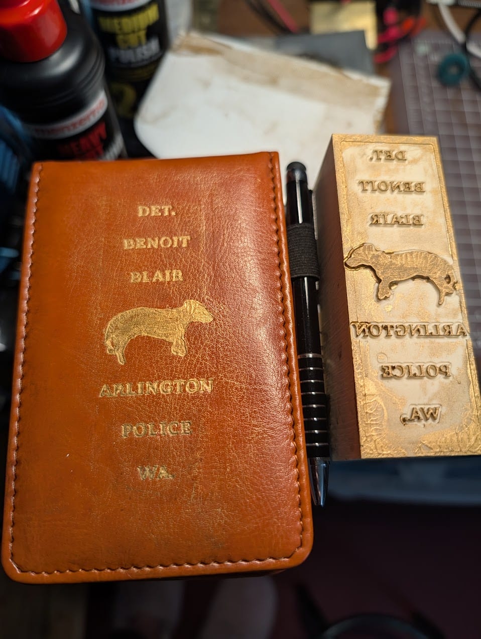 The notebook cover with gold-painted lettering and a dog silhouette, beside the epoxy block used to stamp the paint.