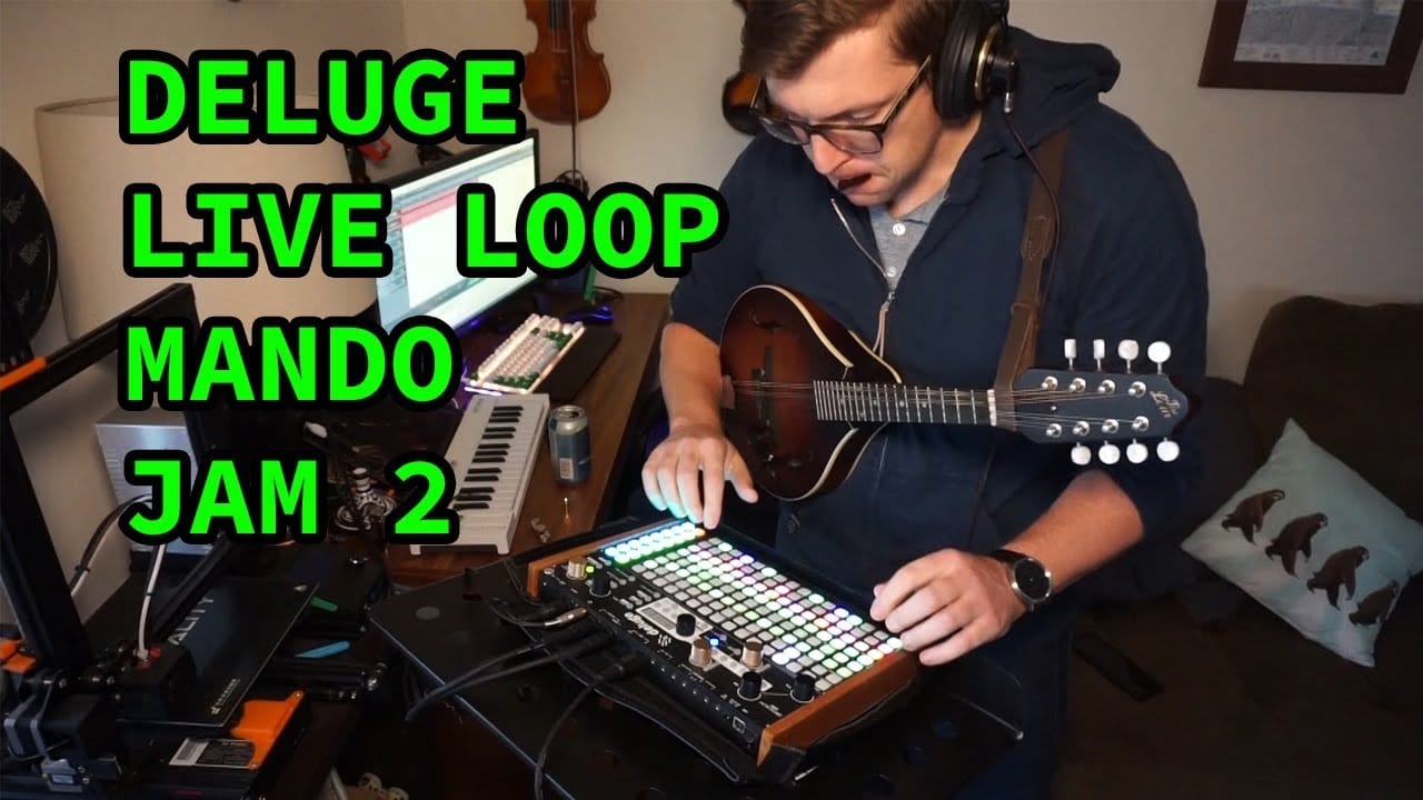 A musician wearing headphones plays a mandolin and works at a lit Deluge beside the words Deluge Live Loop Mando Jam 2.