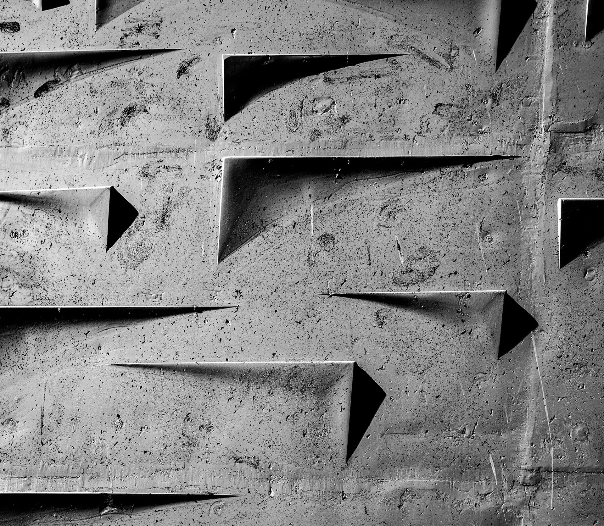 A poured concrete wall in black and white, angular wedges cast into the surface throwing hard shadows.