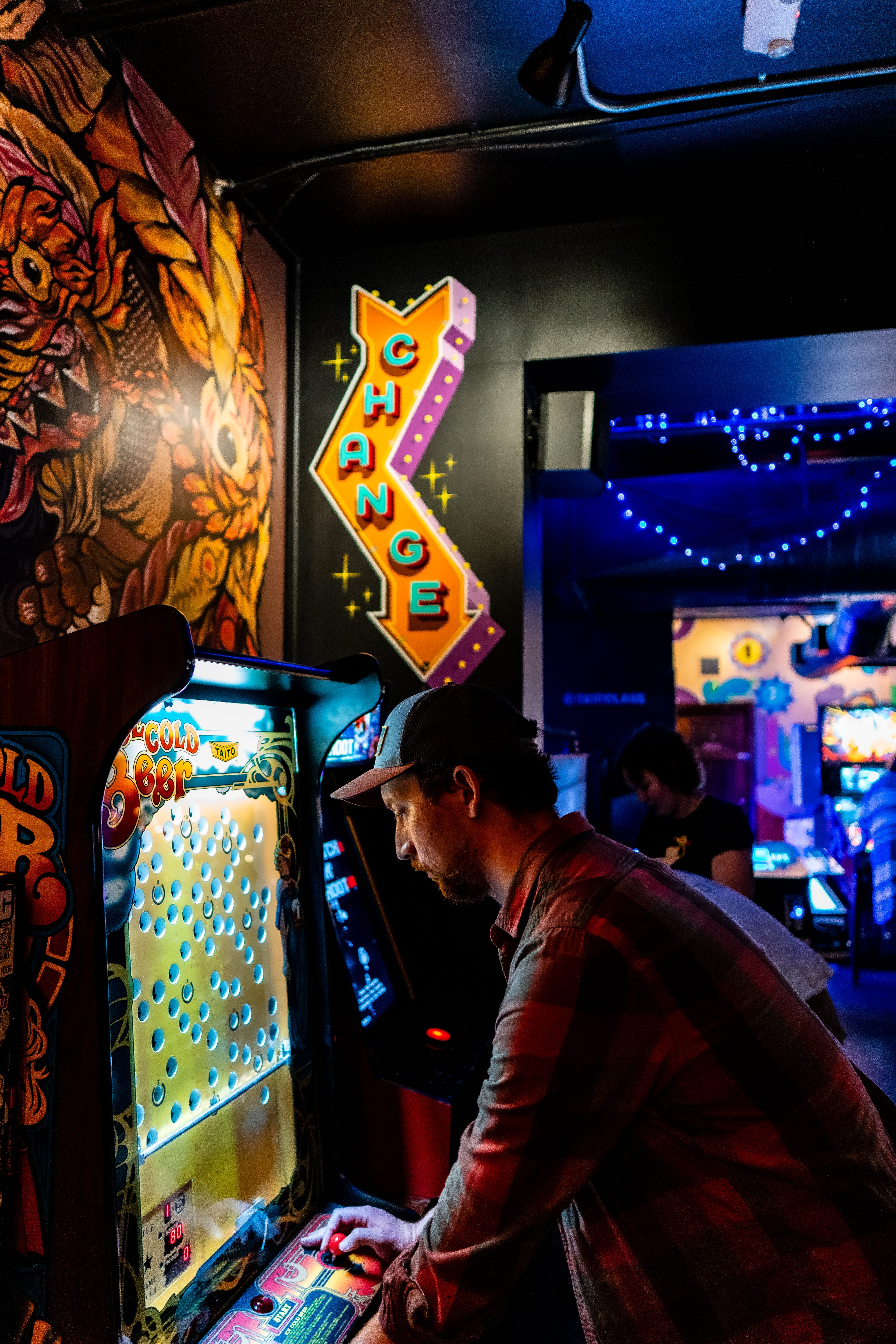 A person plays a brightly lit pinball machine in a dark arcade.
