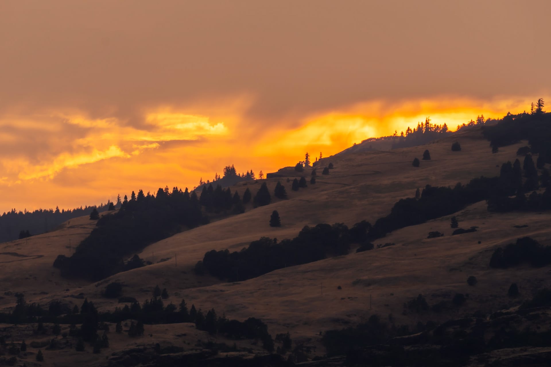 A sunset over dark ridgelines, the sky burning orange above them.