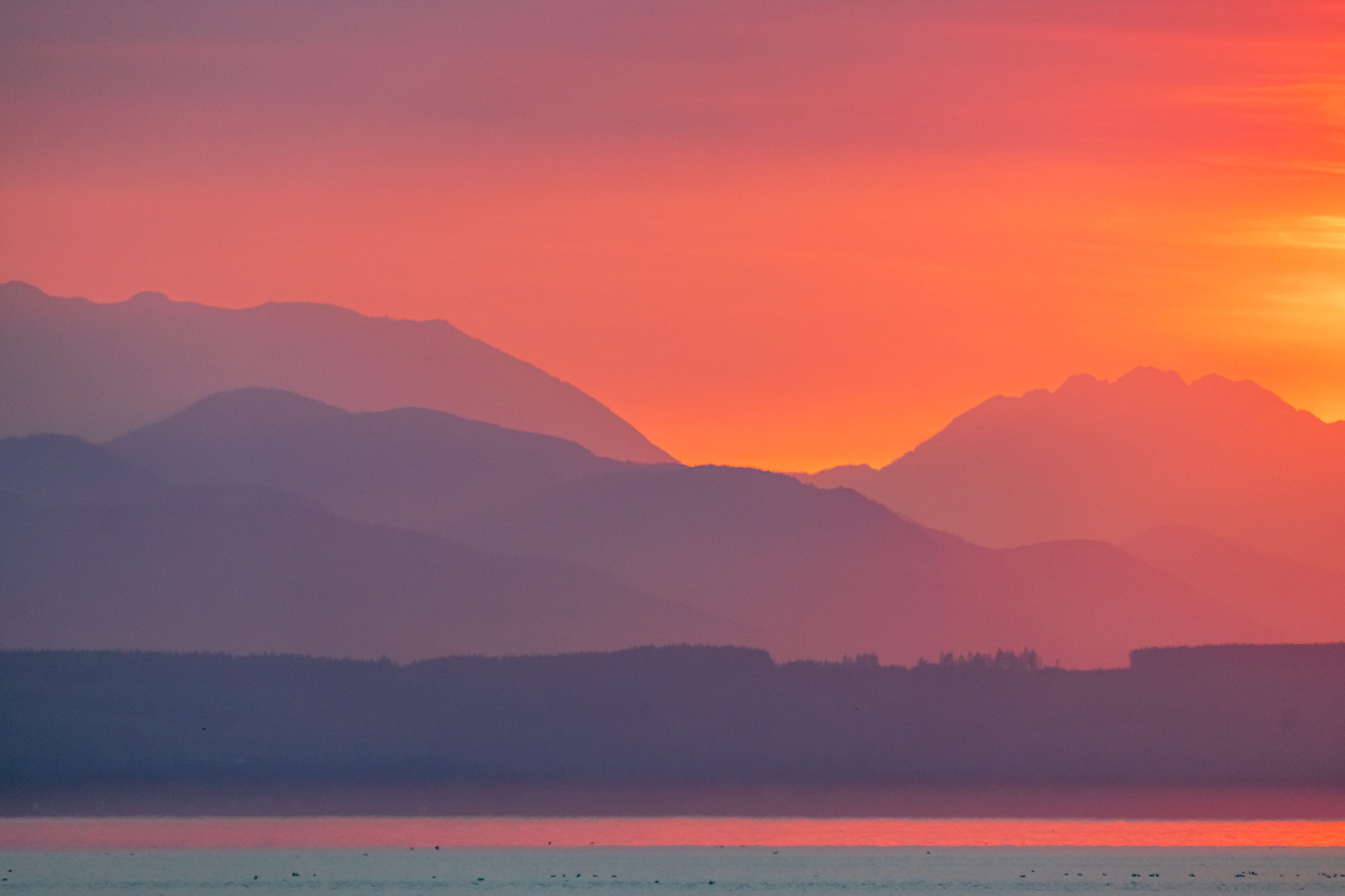 Hazy mountain ridges recede beneath a coral-red sunset sky.