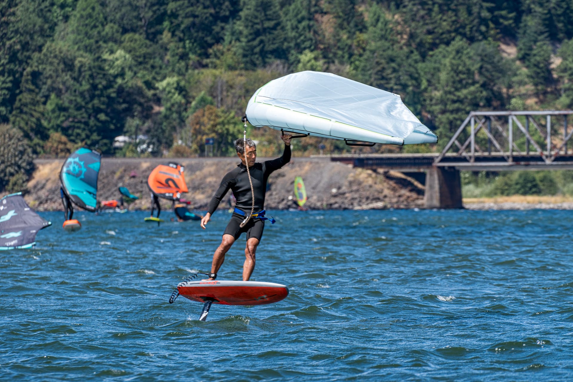 A wing foiler under a white wing, a bridge and other riders behind.