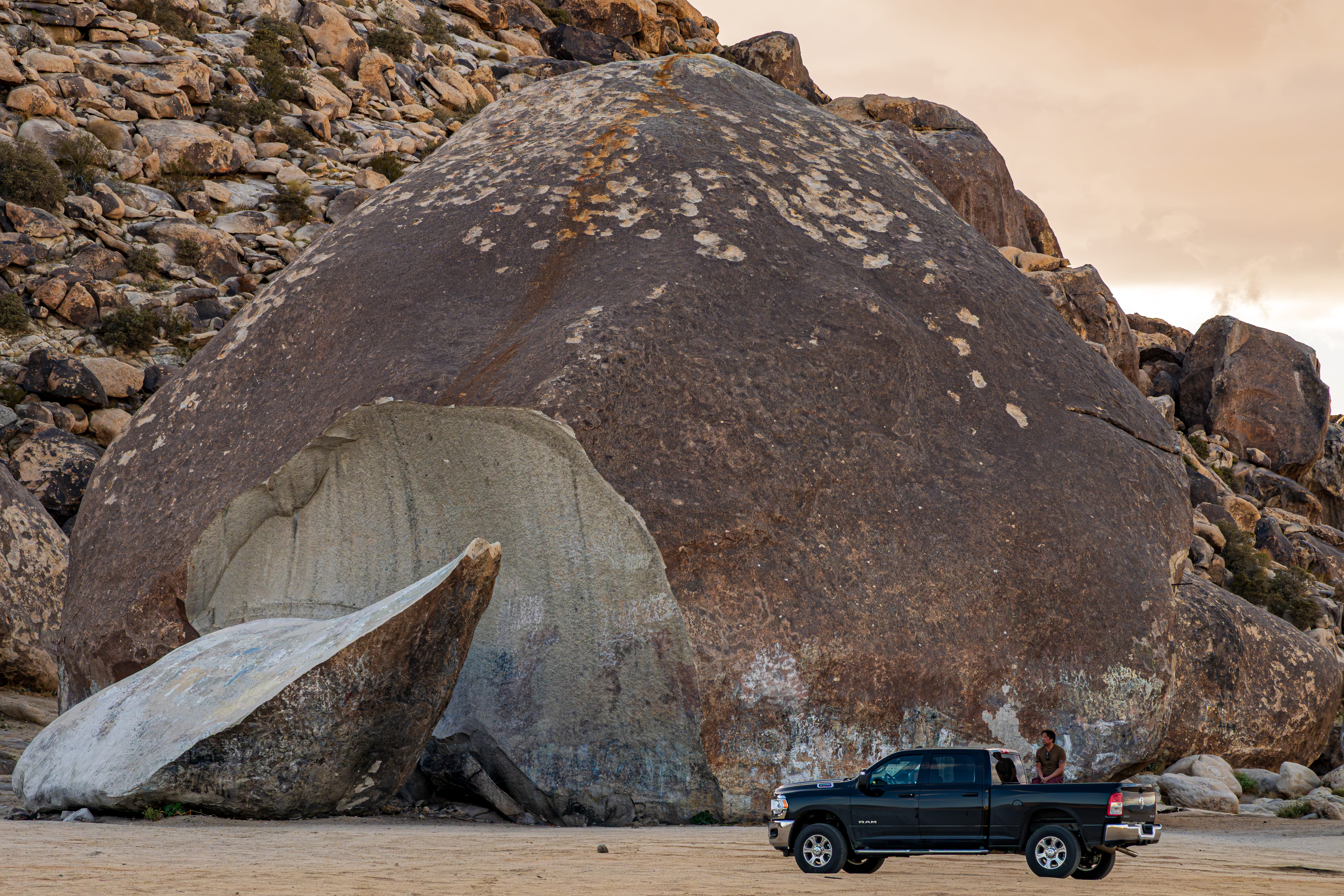 A pickup truck stands beside a massive rounded boulder split by a pale, curved rock face.