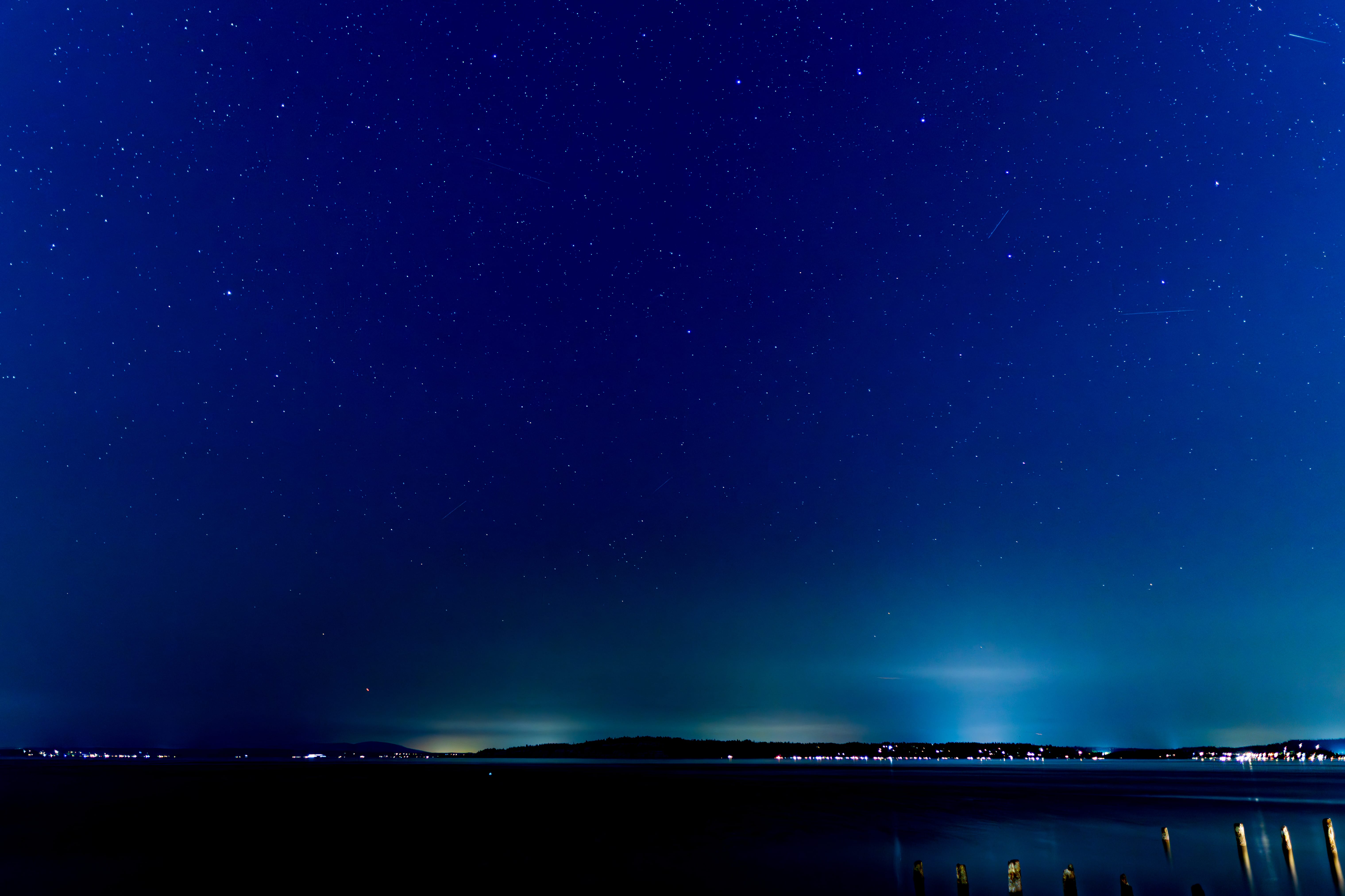 Stars and a faint green glow stretch over a dark shoreline at night.
