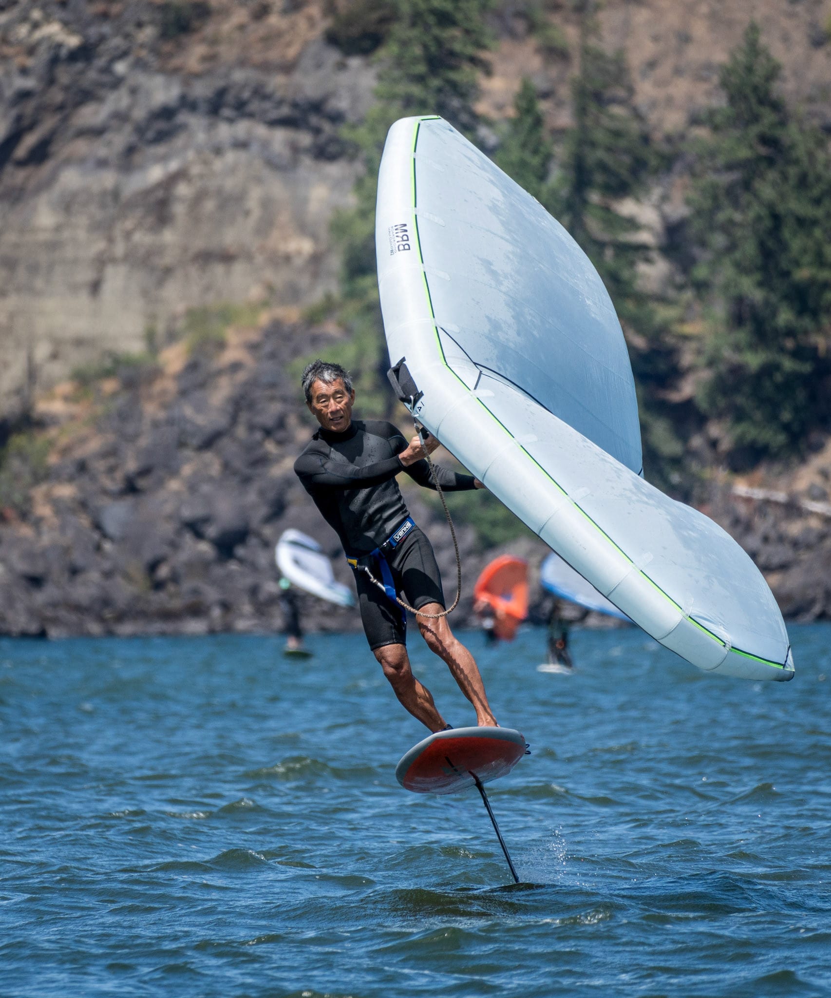 A wing foiler carving on the foil, spray coming off the board.