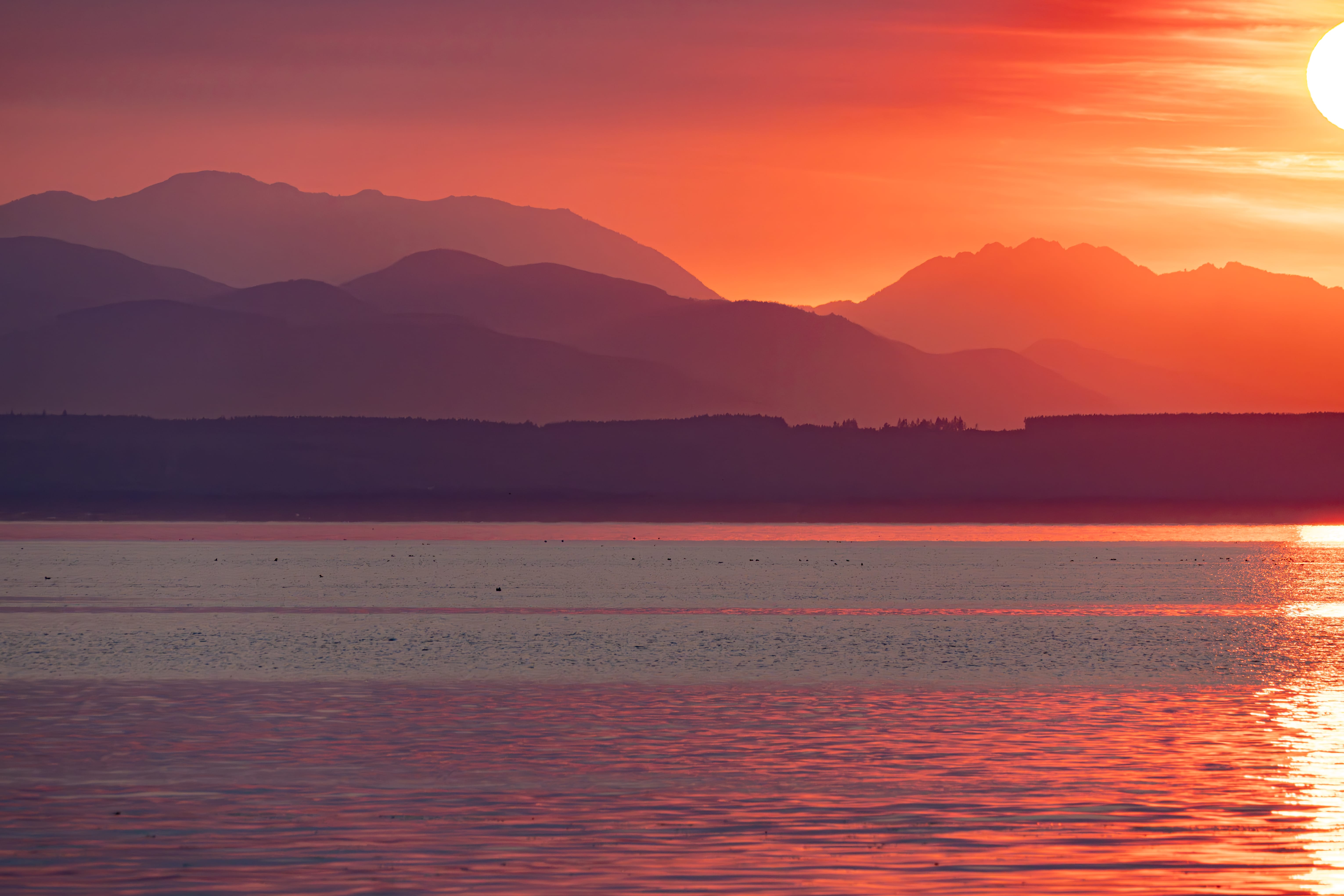 Orange sunset light washes across mountain ridges and a quiet bay.