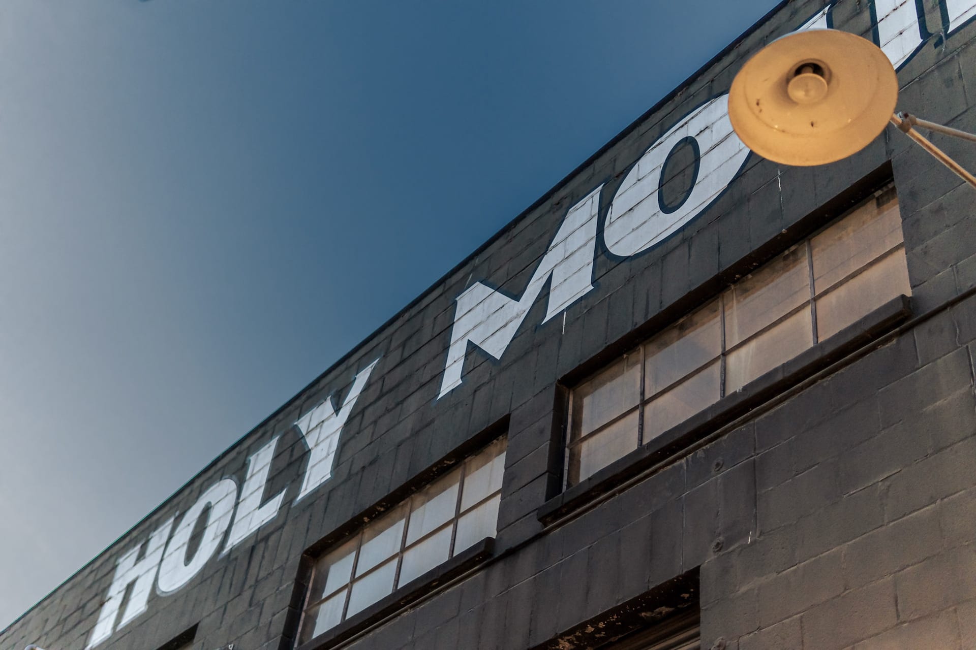 Looking up at the corner of a concrete building with HOLY MO painted across it in tall block letters.