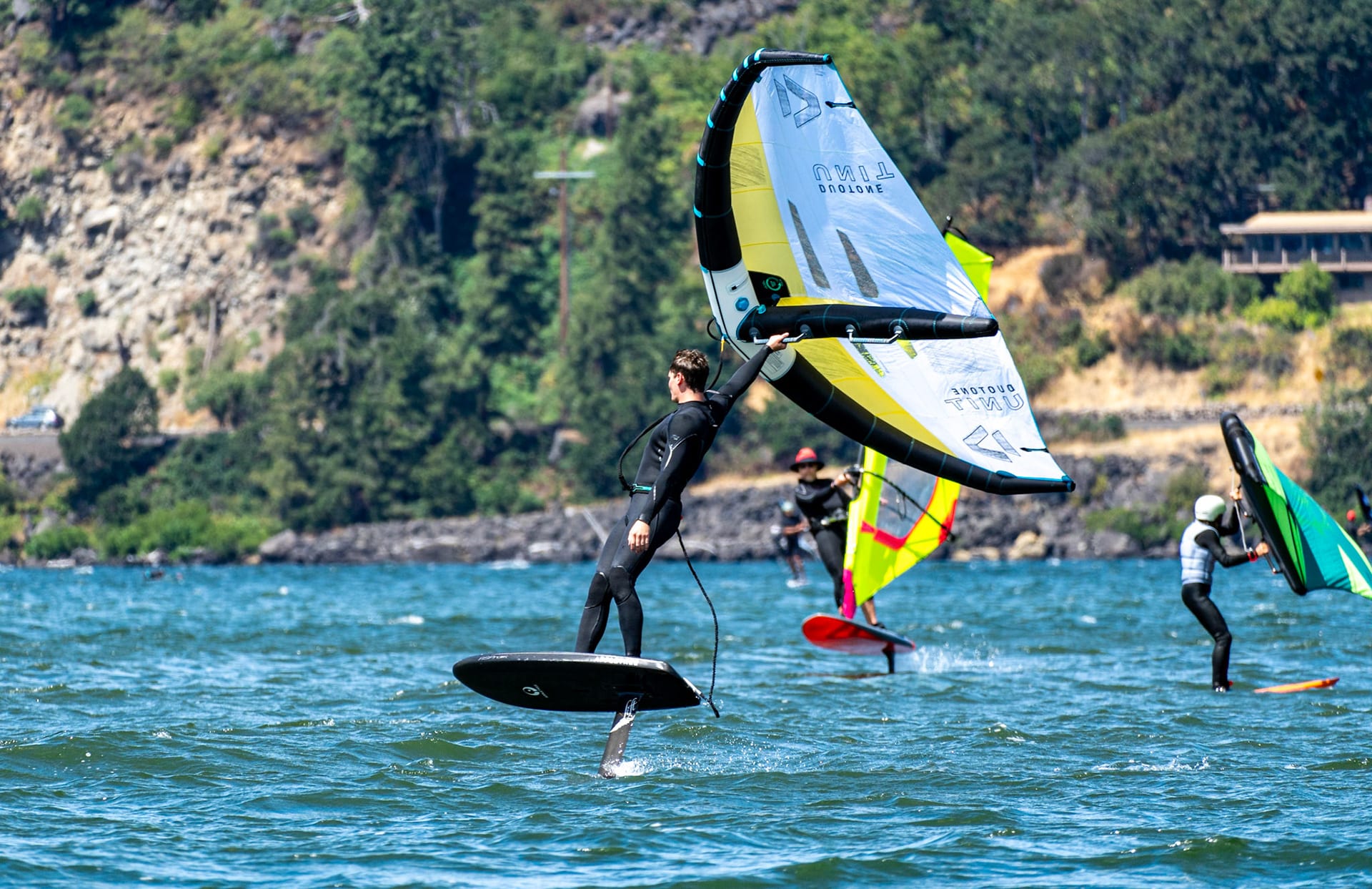 A wing foiler fully up on the foil under a yellow and green wing, cliffs behind.