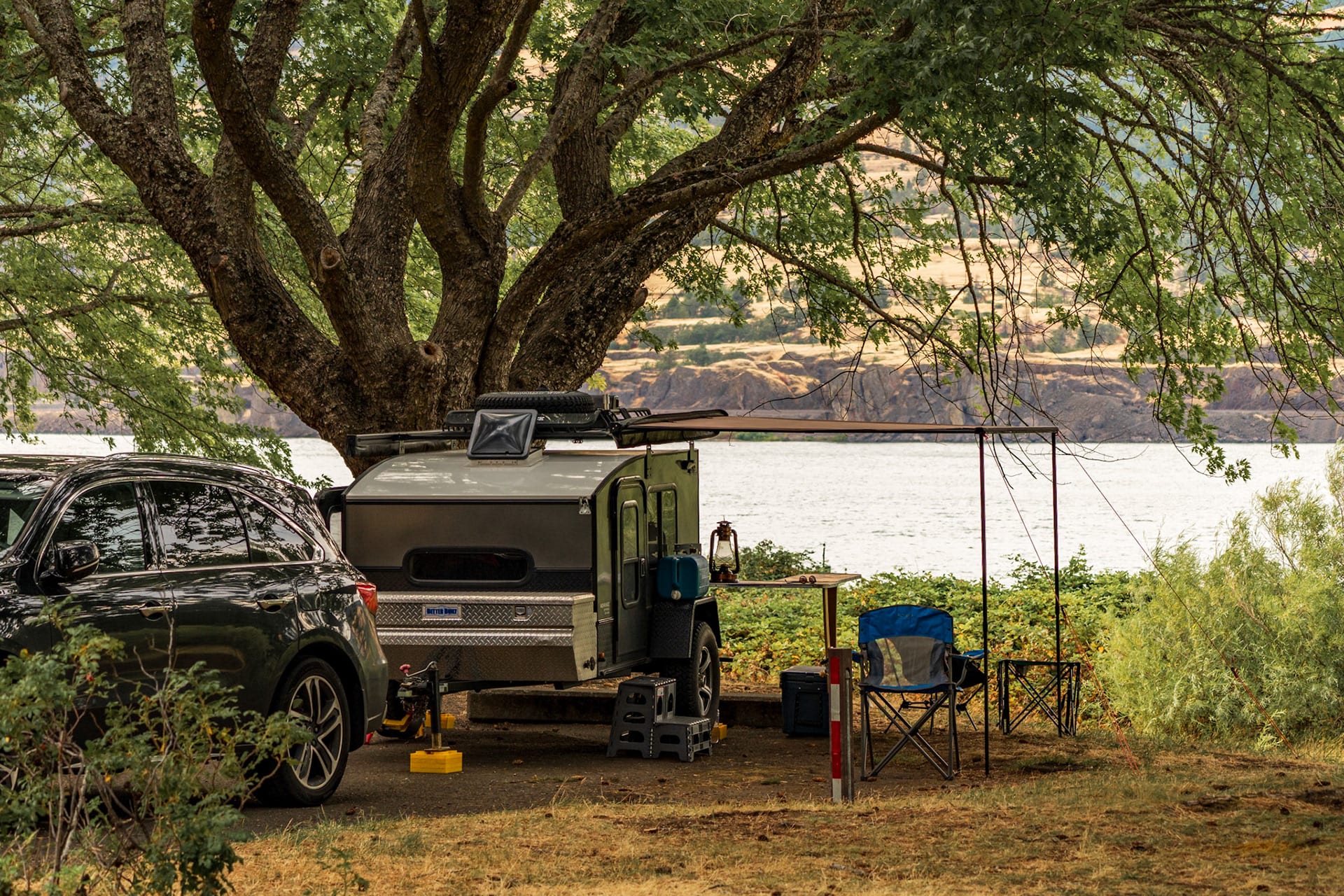 A campsite under a wide spreading oak, a truck parked in the dry grass.
