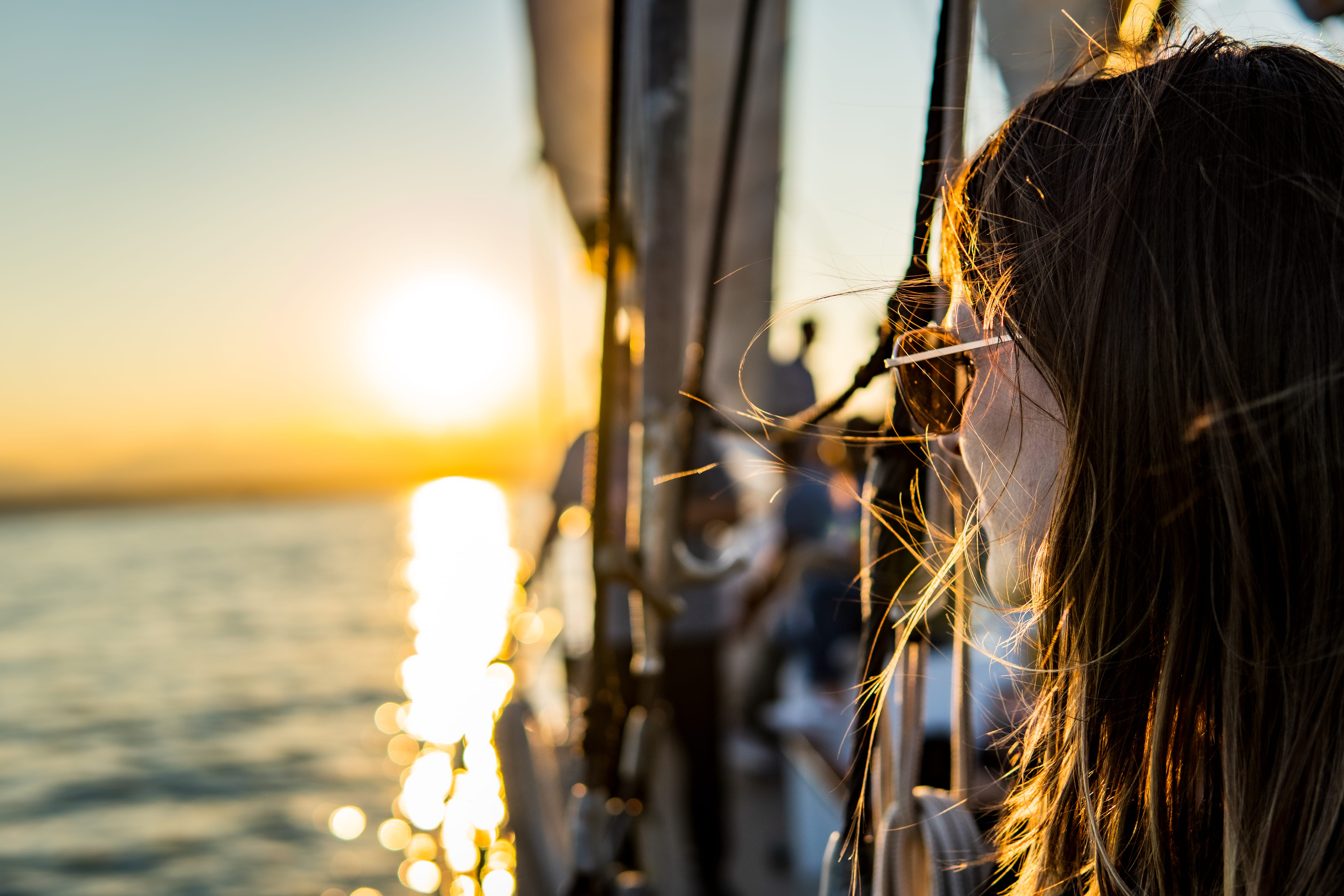 A person watches the sun set over the water from the side of a boat.