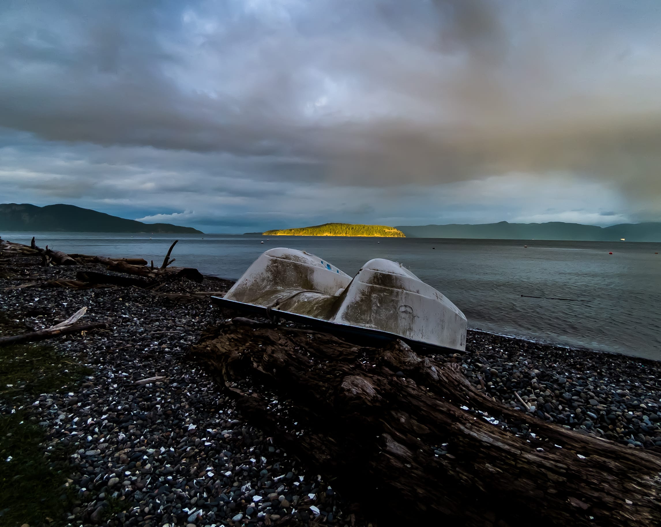 Two overturned boats lie beside driftwood on a dark beach beneath storm clouds.