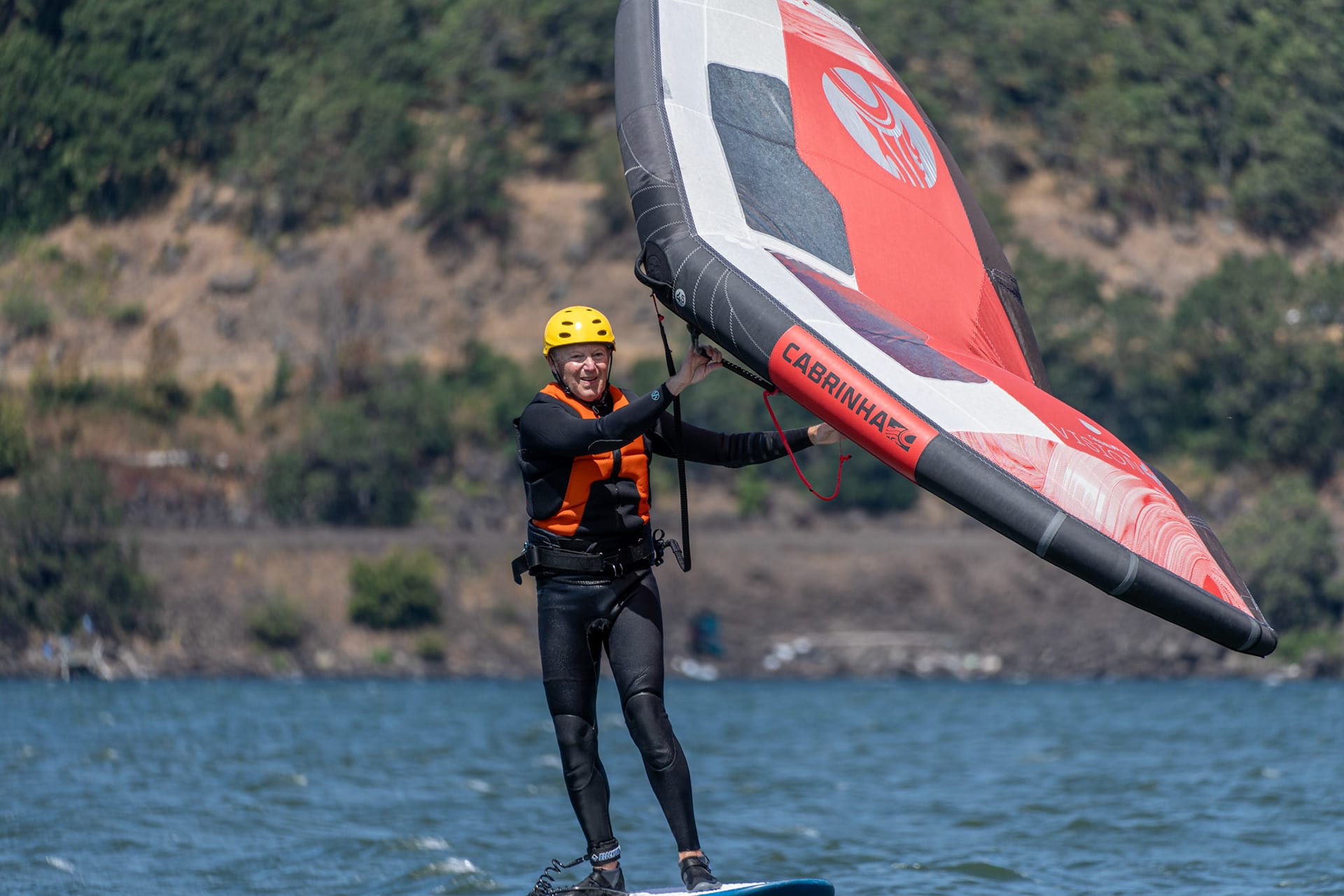 A rider in a yellow helmet lifting a red wing as the board comes up on the foil.