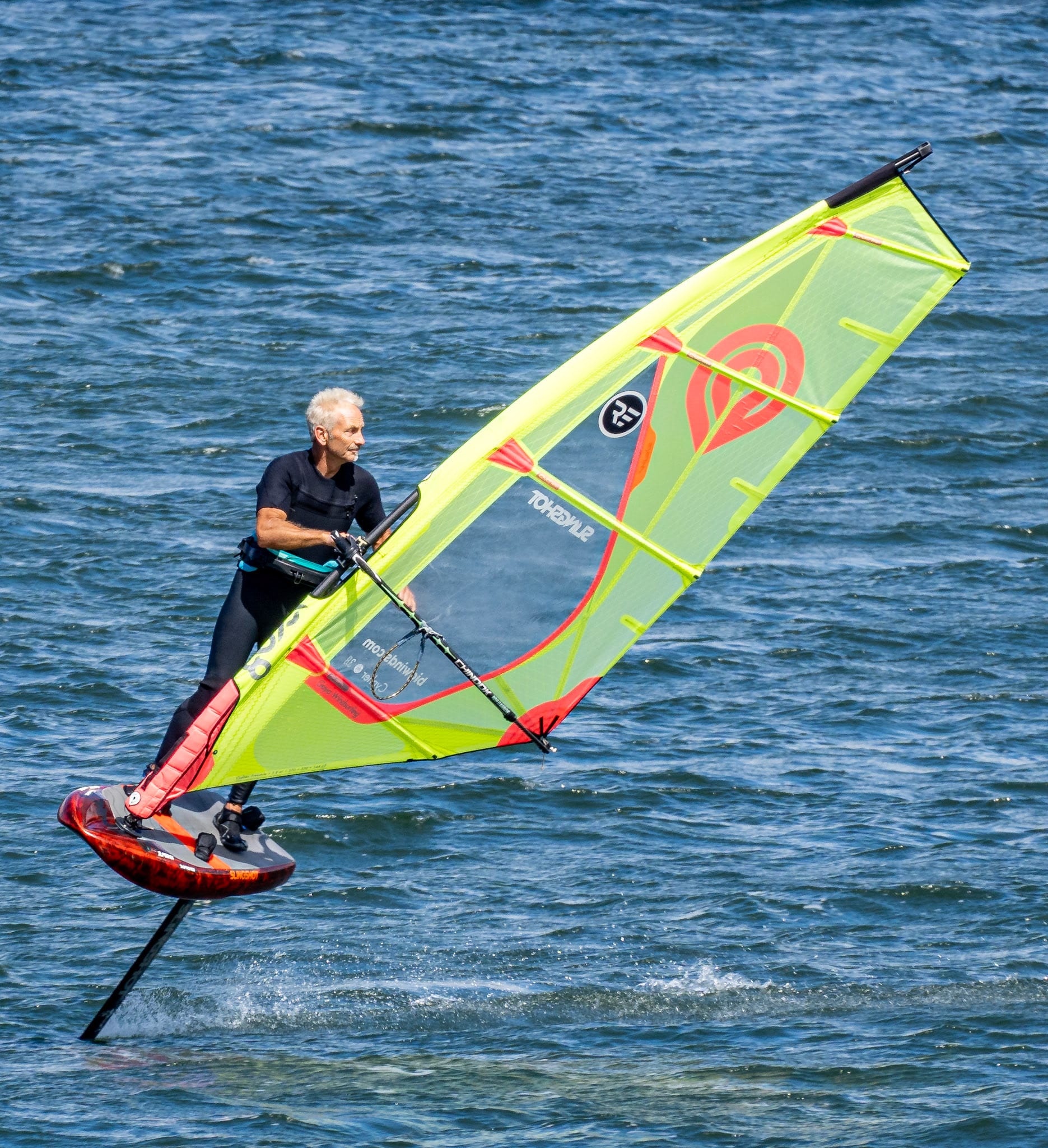A wing foiler holding a yellow and green wing, up on the foil in chop.