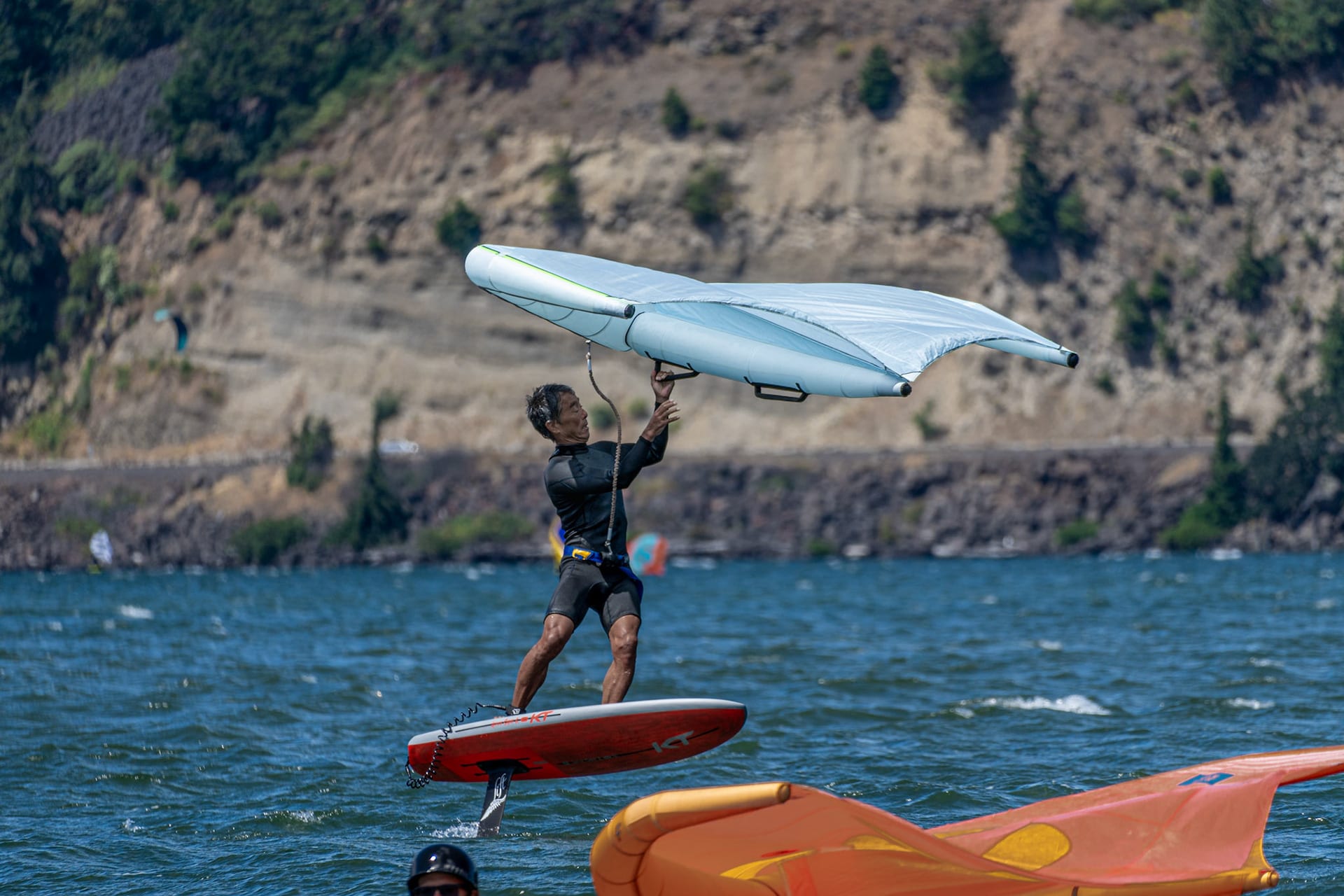 A rider raising a white wing overhead in the water, boards floating nearby.