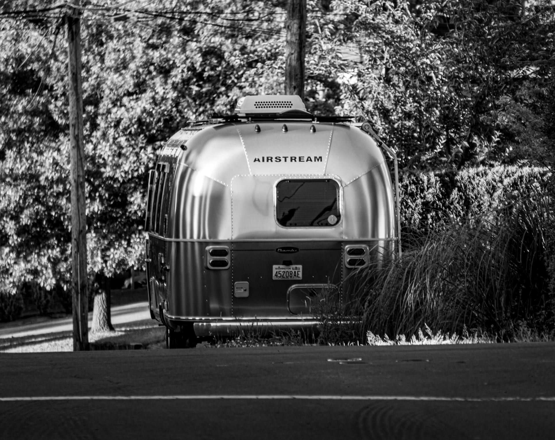 A vintage Airstream trailer parked under trees, in black and white.
