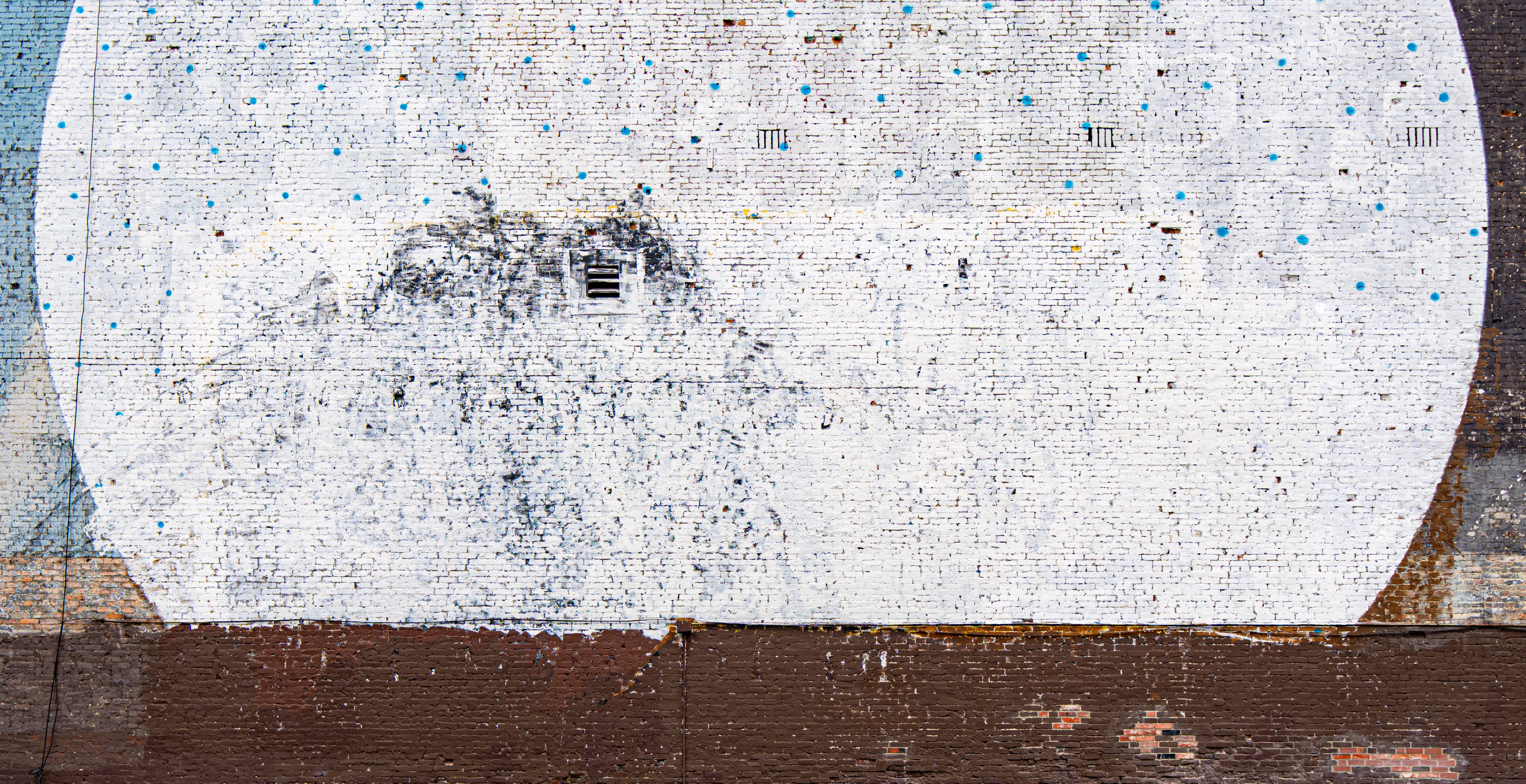 A faded white oval mural with faint face-like marks on a weathered wall.