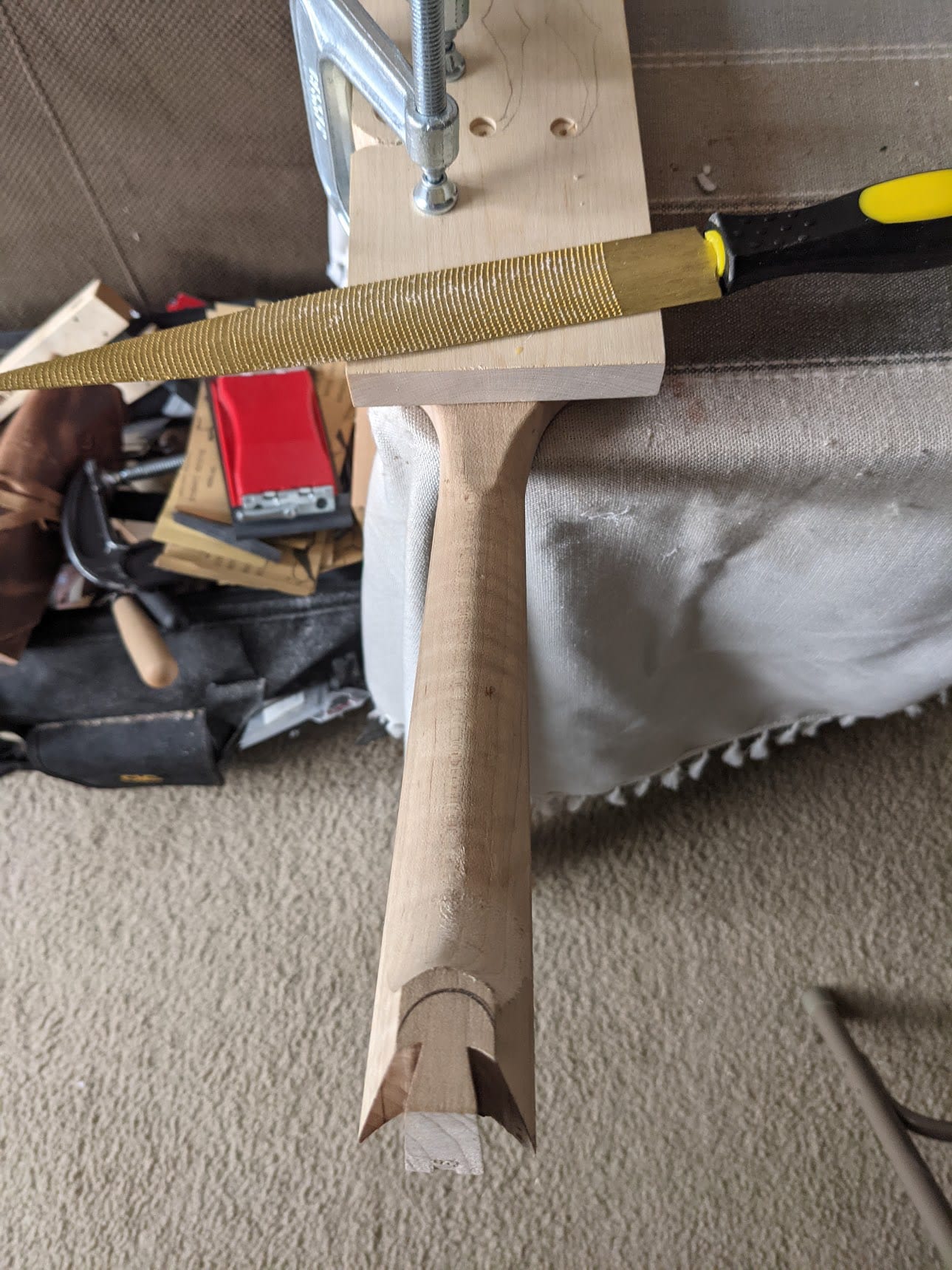 The neck heel being rasped down to the shape of the button, held steady over the bench.