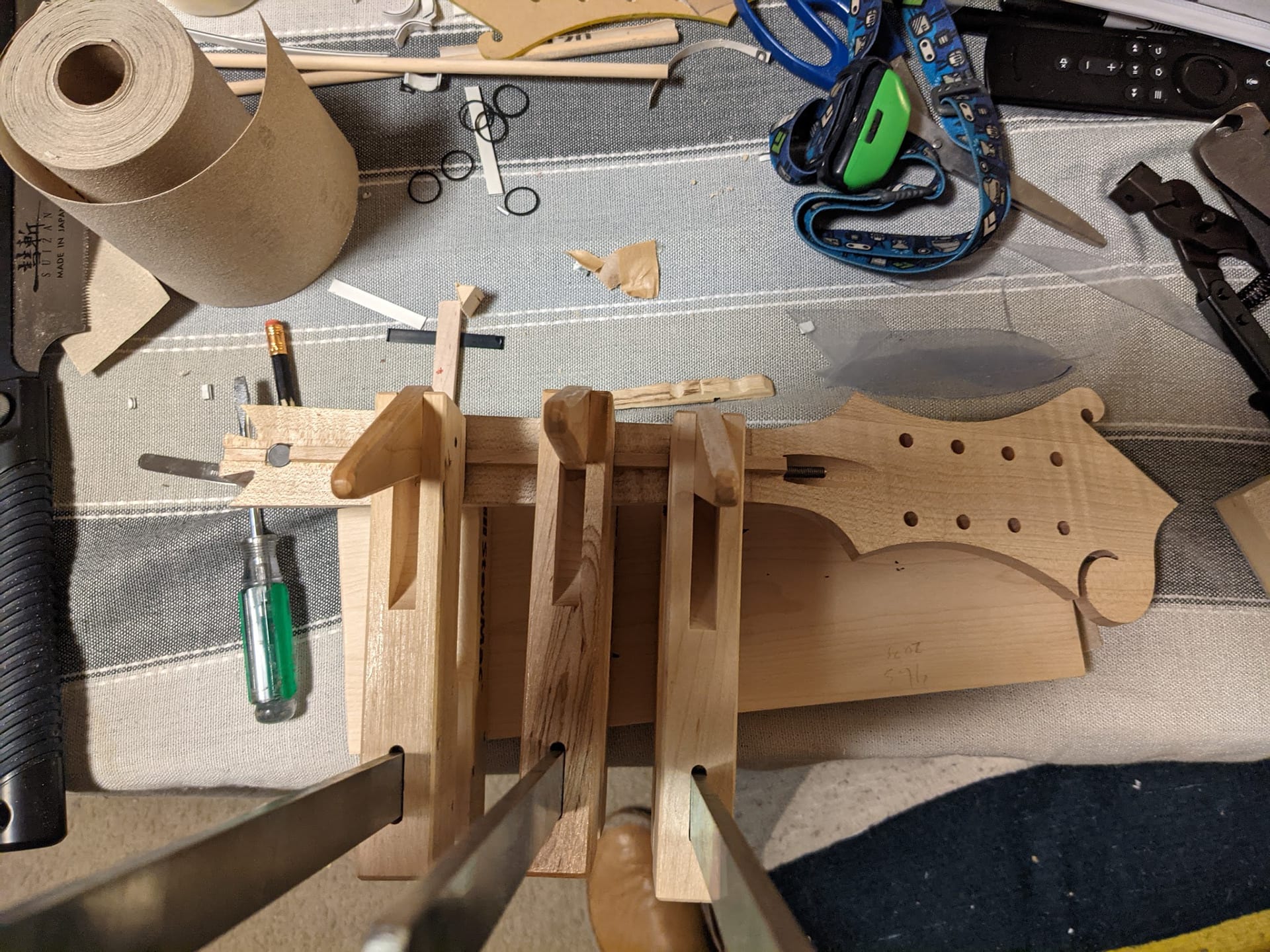 The workbench from above with the neck, a fretboard blank, the razor used to knock the binding down, and a clamping jig.